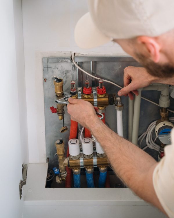 Plumber inspecting pipes in a heating system within a residential boiler room A plumber is carefully checking the pipeline of a heating system in a technical boiler room of an apartment. He is adjusting valves and ensuring proper functionality.