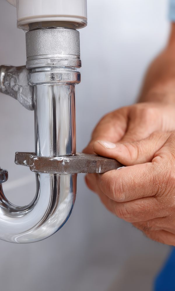 Close-up of a plumber using a wrench to tighten or repair a chrome sink drain pipe, highlighting the plumbing work and maintenance in a bathroom setting. Close-up of a plumber using a wrench to tighten or repair a chrome sink drain pipe, highlighting the plumbing work and maintenance in a bathroom setting.