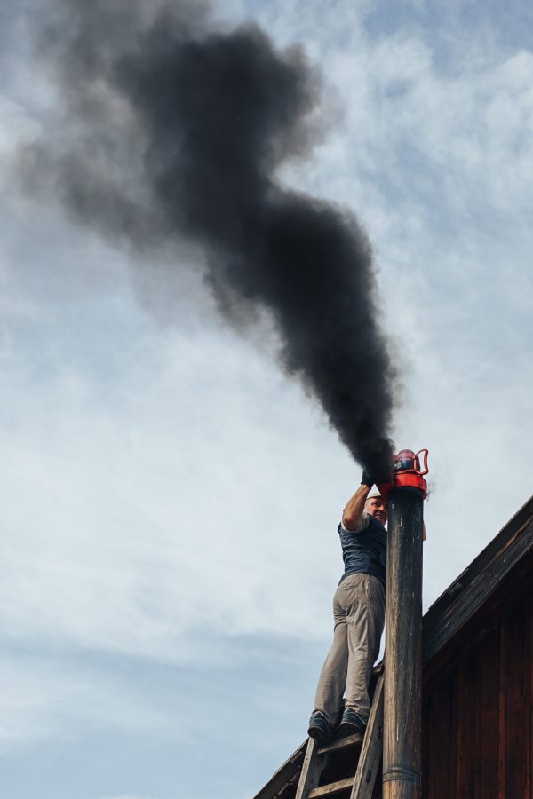 man clean chimney with the help of wacum Chimney sweep cleaning a chimney standing balanced on the apex of a house roof lowering equipment down the flue